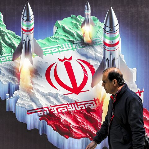 A man walks past a banner depicting missiles launching from a representation of the map of Iran colored with the Iranian flag in central Tehran on April 15, 2024.